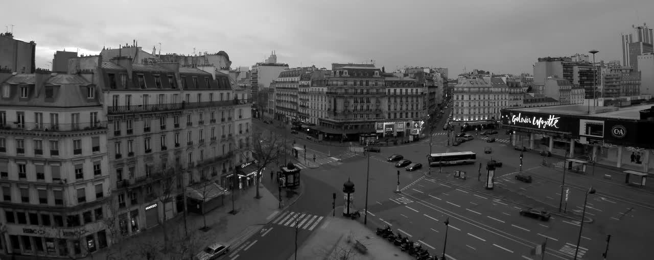Vue plongeante en noir et blanc sur un carrefour parisien : immeubles haussmanniens, boulevards et circulation