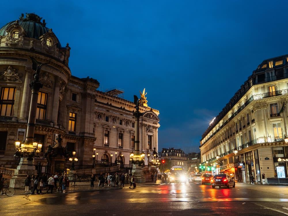 Rue parisienne à l’heure bleue devant la façade illuminée de l’Opéra Garnier