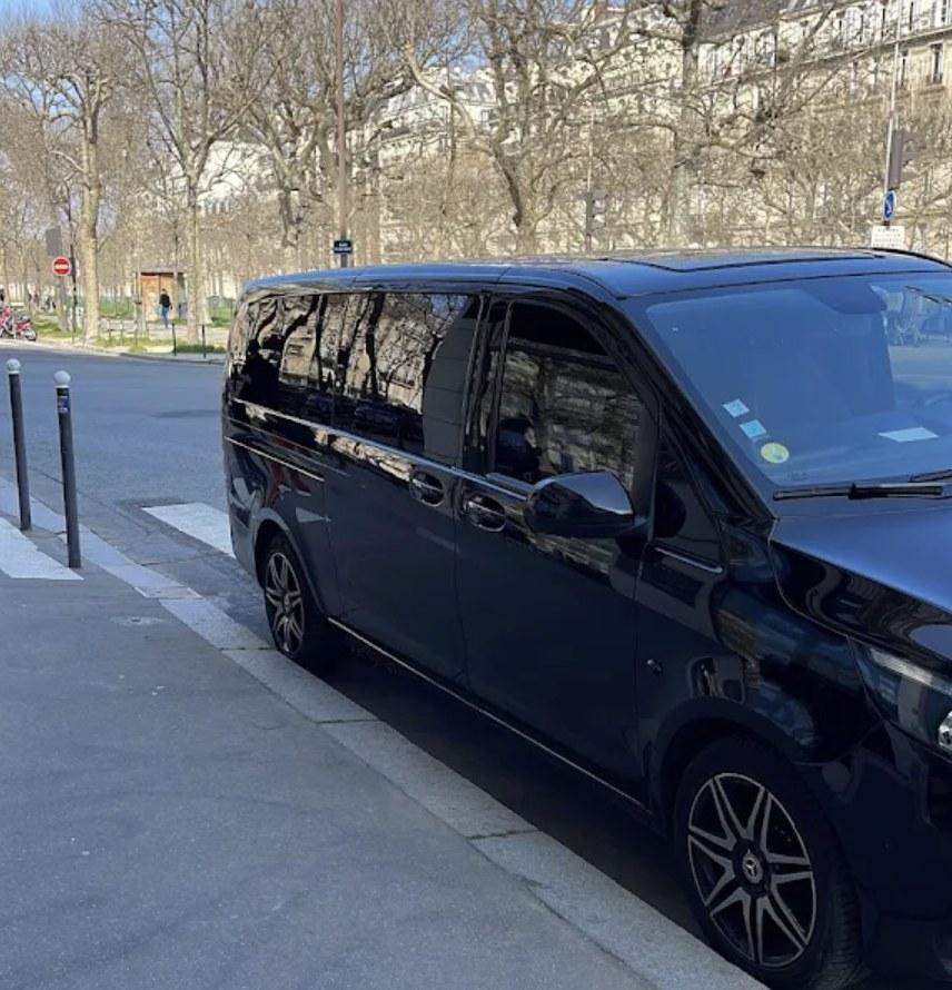 Le van Mercedes-Benz noir de Business Class, vu de trois quarts avant, à l’arrêt le long d’un boulevard parisien bordé de platanes